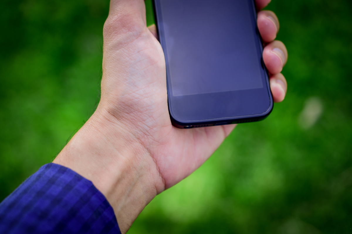 smartfon na tle zieleni w dłoni męskiej